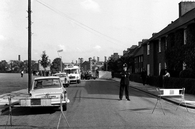 Screens surround the crime scene and a policeman stands guard. The officers, cruising in a police car were shot when they stopped to question men in another car. In the background is Wormwood Scrubs prison. Ref #: PA.3565278  Date: 13/08/1966 