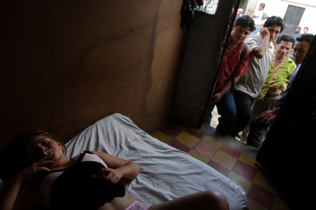 A prostitute from Costa Rica who identifies herself as Angie, 22, smokes a cigarette while clients wait in the doorway of her rented room 