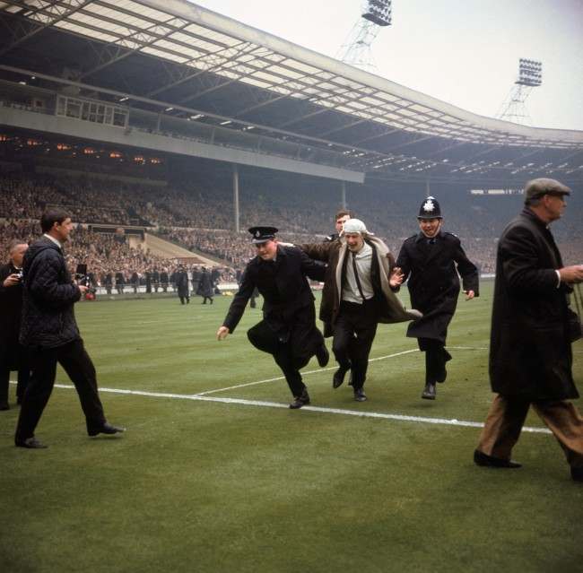 A jubilant Liverpool fan is escorted off the pitch by policemen after running on to celebrate his team's winning goal