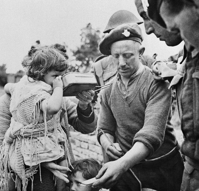 French refugees, including women and children, gather around British soldiers at a Civil Affairs Feeding Center in the Normandy beachhead sector who are supplying hot food on June 16, 1944. Many of the refugees had not eaten for three or more days. (AP Photo)