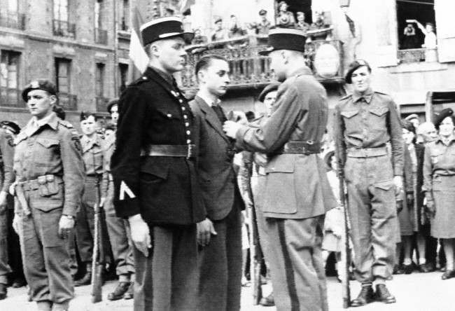 The gendarme (left center) who led the first British troops into Bayeux, and a French underground leader, center, are decorated with the Croix de Guerre during Bastille Day ceremonies in a French city on the Normandy coast, France on July 15, 1944. (AP Photo)