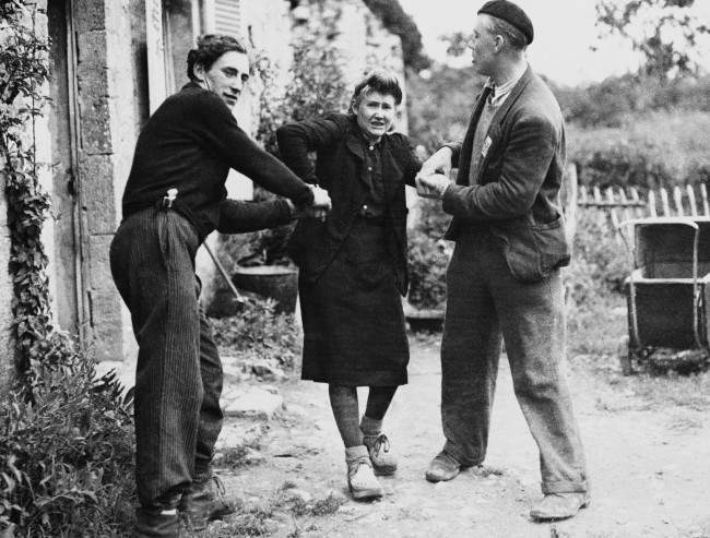 Two French patriots drag Grande Guillotte from her home in Normandy, France on July 10, 1944. After she was discovered to be collaboration with the enemy. The patriots carried through their punishment of the girl by shearing of her hair. (AP Photo)