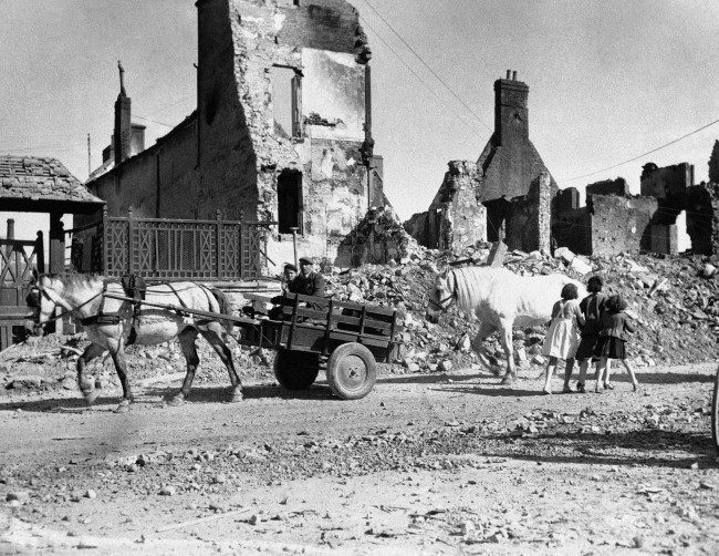 Natives of a French village shattered by the Normandy invasion fighting move down a road past ruined buildings on June 15, 1944. (AP Photo)