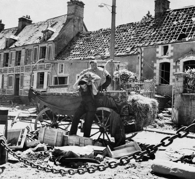 Two French civilian refugees from the battle that raged in St. Sauveur as American troops advanced on Cherbourg on June 23, 1944, unload their cart after returning to their homes. House in background, with most shingles gone. (AP Photo)