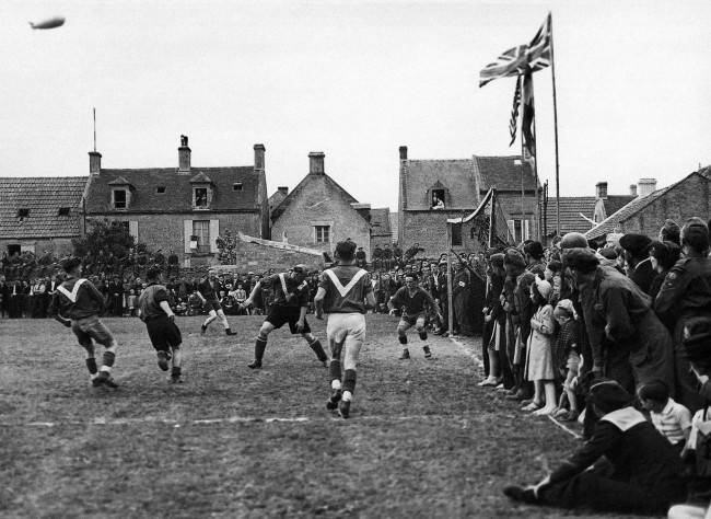 For the first time since 1939, French men and women in the liberated towns and villages of Normandy were able openly to celebrate on July 14th, Bastille Day, without fear of German reprisals. In the little town of Coursoulles near the coast, where this picture was taken in July 1944, British troops played a football match against the local French team and all the towns folk turned out to watch the game. The match in progress with enthusiastic spectators crowding the touch-line. (AP Photo/Photographic News Agencies, LTD.)