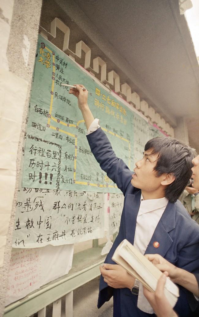 A student at Beijing University points to a map of the march route on a poster up on campus as he recounts a tale of how marchers pushed through police lines on their way to Tiananmen Square, April 28, 1989. (AP Photo/Mark Avery)