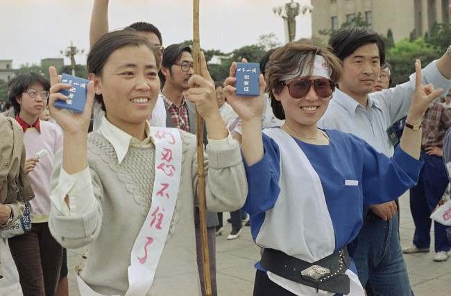 Employees of CCTV, Central China Television, flash their press cards as they join student strikers for democracy in Beijing's Tiananmen Square at night, Tuesday, May 16, 1989. (AP Photo/ Sadayuki Mikami)