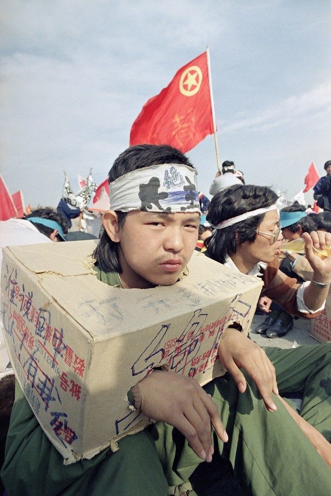 A Beijing university student sits bound in a cardboard box as the strike for democracy continues for the third day in Beijing's Tiananmen Square, Tuesday, May 16, 1989. The box indicates he cannot use his hands so he cannot eat. (AP Photo/Sadayuki Mikami)