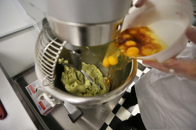 Eggs are added into a mixer with green cannabis-infused "canna butter" in a stainless steel bowl at the start of batter mixing for peanut butter jelly cups