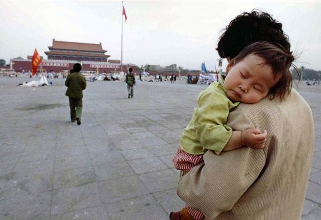 A child sleeps on his mother's shoulder as she crosses Tiananmen Square, Beijing, on May 29, 1989. Many students have tired and returned to their classes following three weeks of pro-democratic rallies. (AP Photo/Staff/Widener)