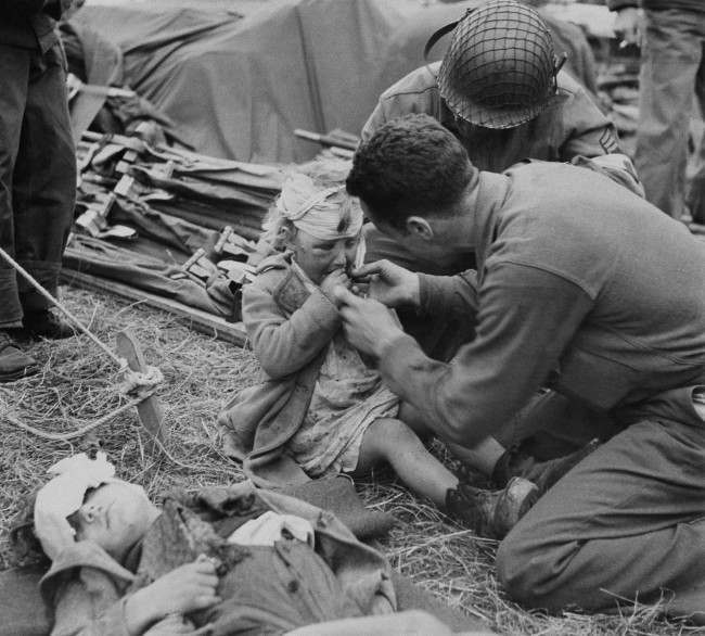 American Army medical corpsmen try to assuage the grief of a little French girl with a gift of candy in France, June 17, 1944. Her head is bandaged and face swollen. Another child lies in front with his head bandaged. Both youngsters are evidently under the effects of the terror of Normandy. (AP Photo)