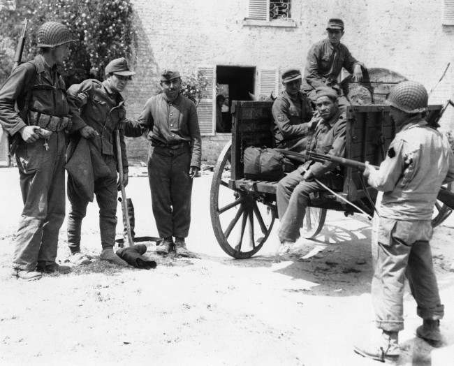 An American soldier and a French peasant assist a wounded Nazi prisoner into a cart in which he and others captured in a small French village, in Normandy, on June 10, 1944, were transported back to the beach en route to England and internment. (AP Photo)