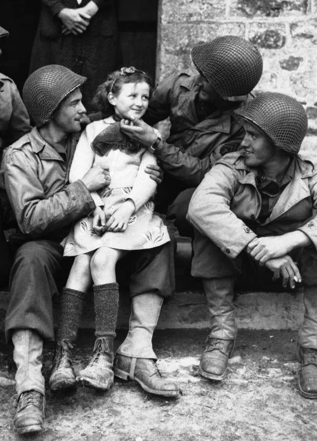 A little French girl finds three admirers from the ranks of American forces who have made a speedy and successful advance through Normandy, France on June 22, 1944. From left to right,Private Robert D. Furra, Private Willie Johnson and Private C.K. Jones. (AP Photo)