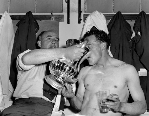 Bolton Wanderers captain and centre-forward Nat Lofthouse, who scored both his team's goals, is given a drink from the FA Cup by manager Bill Ridding in the dressing room at Wembley after Bolton had beaten Manchester United 2-0 in the Cup Final.