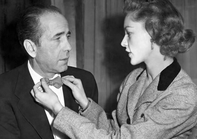 Actress Lauren Bacall, 27, adjust the bowtie of her husband Humphrey Bogart, 50, at a reception in Claridge's Hotel, London. Date: 16/04/1951