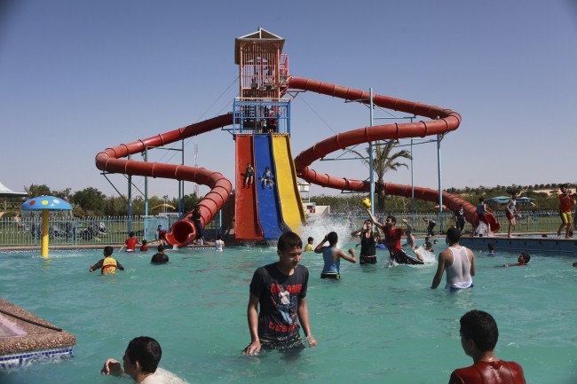 Palestinian boys play on a water slide as others have a sunbath at a swimming pool in Asdaa city, Khan Younis, southern Gaza Strip, Monday, April 28, 2014. (AP Photo/Adel Hana)