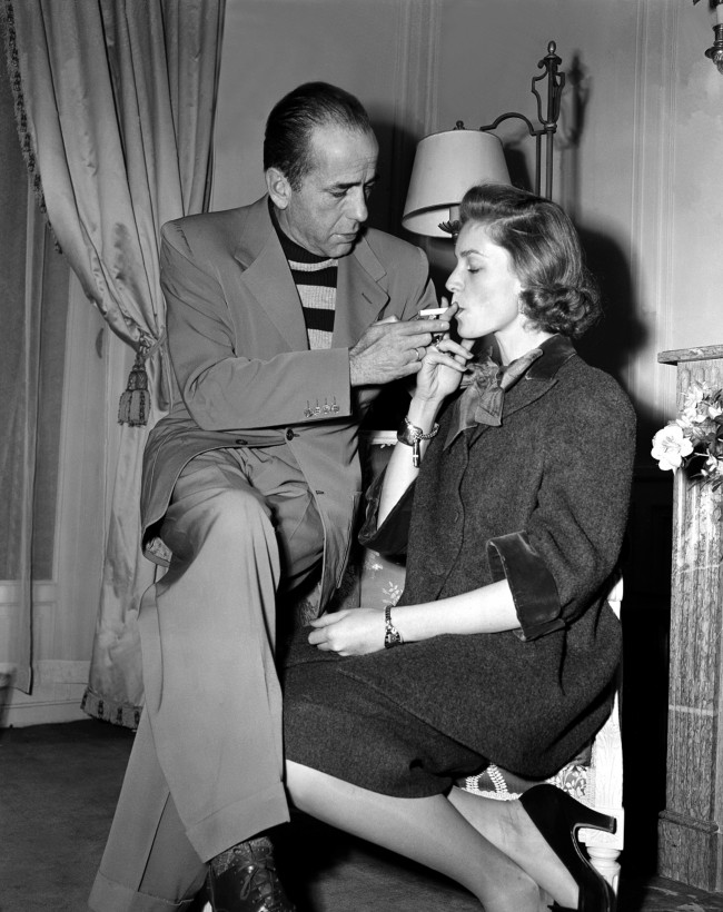 Actor Humphrey Bogart lights a cigarette for his wife, actress Lauren Bacall, in their room at the Ritz Hotel in Paris, France, during their vacation on March 26, 1951.