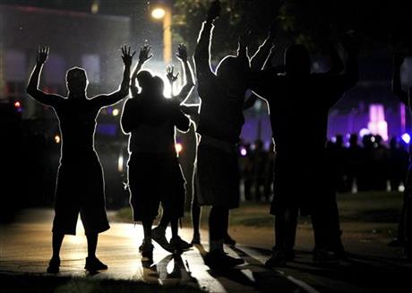 People raise their hands in the middle of the street as police wearing riot gear move toward their position trying to get them to disperse Monday, Aug. 11, 2014, in Ferguson, Mo. The FBI opened an investigation Monday into the death of 18-year-old Michael Brown, who police said was shot multiple times Saturday after being confronted by an officer in Ferguson. Authorities in Ferguson used tear gas and rubber bullets to try to disperse a large crowd Monday night that had gathered at the site of a burned-out convenience store damaged a night earlier, when many businesses in the area were looted. (AP Photo/Jeff Roberson)
