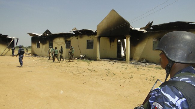 In this photo taken on Monday, Oct. 28, 2013, police and soldiers stand in front of a burnt out army barracks following an attack by Boko Haram in in Damaturu, Nigeria. Nigerian military and hospital reports indicate a 5-hour-long battle between Islamic extremists and troops in the capital of NigeriaÂs Yobe state last Thursday and Friday killed at least 90 militants, 23 soldiers and eight police officers. (AP Photo)
