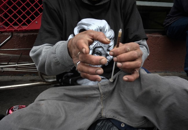 In this Monday, May 6, 2013 file photo, a drug addict prepares a needle to inject himself with heroin in front of a church in the Skid Row area of Los Angeles. The death of actor Philip Seymour Hoffman in February 2014 spotlighted the reality that heroin is no longer limited to the back alleys of American life. Once mainly a city phenomenon, the drug has spread to the country and suburbs. (AP Photo/Jae C. Hong)