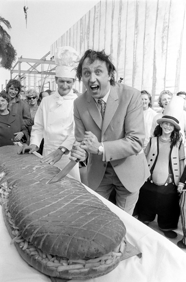 Comedian Ken Dodd cuts into a six-foot long "chip butty" claimed to be world's biggest. It was presented to him to-day when he officially opened new extensions to a frozen chip factory in Scarborough, Yorkshire.  Ref #: PA.18058690  Date: 16/09/1970