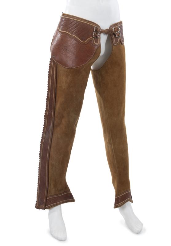 Estimate: $200 - $300 Starting: $100 A pair of Burt Reynolds brown leather chaps. Dark brown trim is tooled to look as though the leather was woven. Additional floral tooling, lacing and buckle closure and faux bone fasteners down the side of each leg.