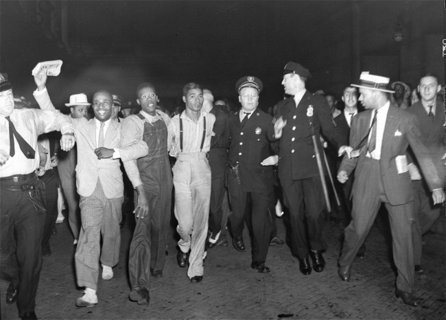 In this July 26, 1937 file photo, police escort two of the five recently freed "Scottsboro Boys," Olen Montgomery, wearing glasses, third left, and Eugene Williams, wearing suspenders, forth left through the crowd greeting them upon their arrival at Penn Station in New York. In a final chapter to one of the most important civil rights episodes in American history, Alabama lawmakers voted Thursday, April 4, 2013, to give posthumous pardons to the "Scottsboro Boys": nine black teens who were wrongly convicted of raping two white women in 1931. (AP Photo, File)