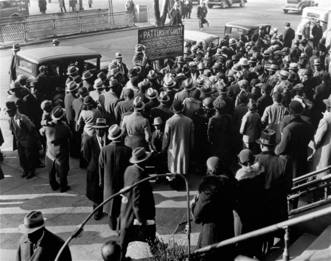 Residents gather in Harlem, New York City, April 9, 1933, to read a placard protesting against the decision of a jury in the trial of Haywood Patterson, one of the nine Scottsboro Boys to be indicted, at Decatur, Ala. Patterson was found guilty of assault against two white girls near Scottsboro, Ala. about two years ago. (AP Photo)
