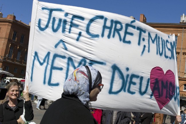 People gather to pay their respects to the shooting victims of Mohamed Merah in Toulouse, France, Friday March 23, 2012. France's prime minister fended off suggestions Friday that anti-terrorism authorities fell down on the job in monitoring a radical Islamist who gunned down children, paratroopers and a rabbi in a wave of killings that revolted the country. Merah, who claimed allegiance to al-Qaida died Thursday during a gunfight with police following a 32-hour standoff outside his apartment in the southwestern city of Toulouse. Banner reads:" Jews, Christians, muslims, same God, Love". (AP Photo/Thibault Camus)