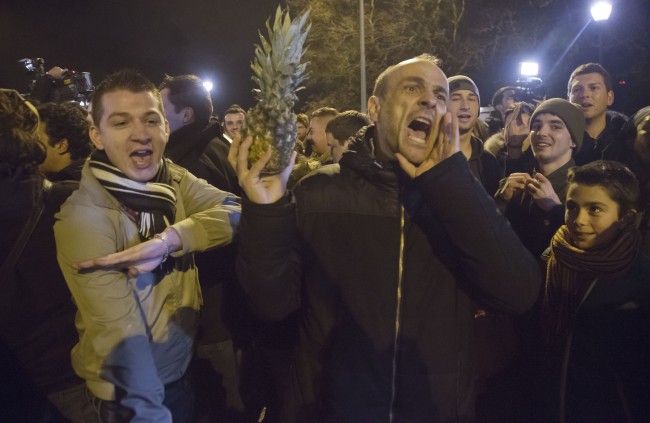 People making the ÂquenelleÂ hand gesture, which French Interior Minister Manuel Valls has criticized as an "inverted Nazi salute" and holding a pineapple outside the Zenith arena where French comic Dieudonne's show was banned in Nantes, France, Thursday, Jan. 9, 2014. The French comic who is considered anti-Semitic was banned from performing Thursday night just hours after a court in Nantes said he could go ahead with his show. The comic was convicted last fall for using the word "Shoananas," a mash-up of the Hebrew word for Holocaust and the French word for pineapple. (AP Photo/Michel Euler)