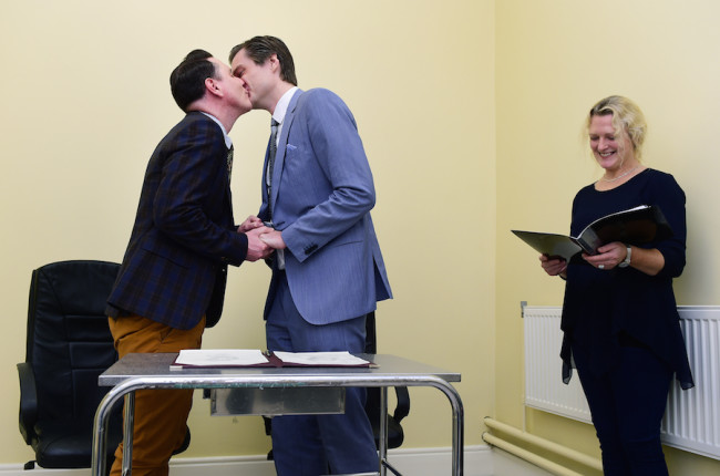DUBLIN, IRELAND - NOVEMBER 17:  Newly married couple Richard Dowling (L) and Cormac Gollogly (2nd L) kiss next to registrar Mary Clare Heffernan (R) after the first ever same sex marriage takes in Clonmel on November 17, 2015 in Dublin, Ireland. Irish officialdom began recognising same sex marriage on Monday, following passage of the Marriage Act 2015 which was a result of the referendum on same sex marriage held earlier this year. This mornings ceremony took place in a small waiting room outside the registrar office at Clonmel Community Care Centre to ensure that this was the first same sex marriage.  (Photo by Charles McQuillan/Getty Images)