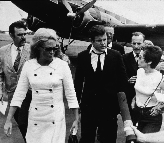 Reporters question American Senator Edward Kennedy (center, with neck brace) and his wife Joan Kennedy (left, in white coat and dark glasses) as they walk across the tarmac after returning from the funeral of Mary Jo Kopechne, Hyannis, Massachusetts, July 22, 1969. Kopechne died when a car driven by Kennedy went over the side of a bridge on Chappaquiddick Island four days earlier. (Photo by Hulton Archive/Getty Images)