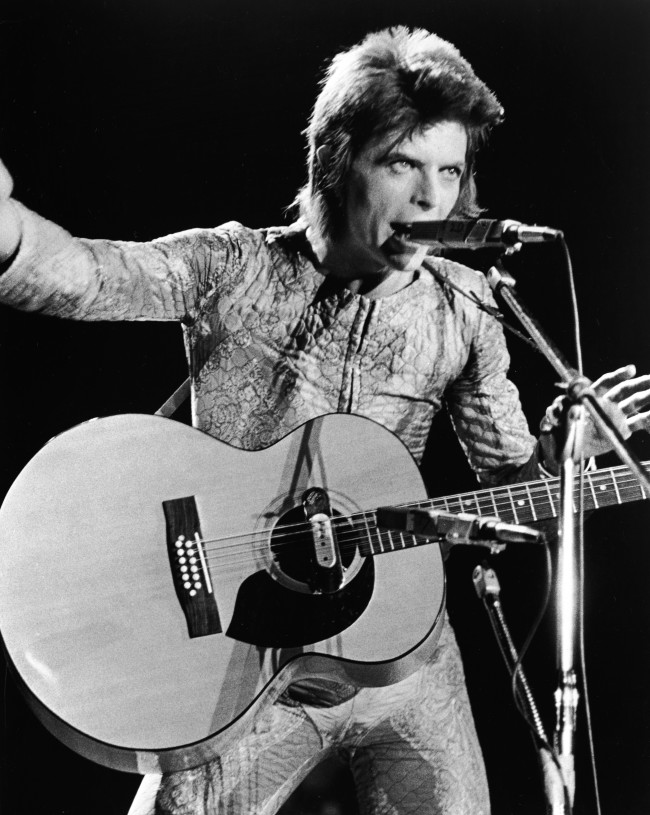 British rock singer David Bowie performs with an acoustic guitar on stage, in costume as 'Ziggy Stardust,' circa 1973. (Photo by Hulton Archive/Getty Images)
