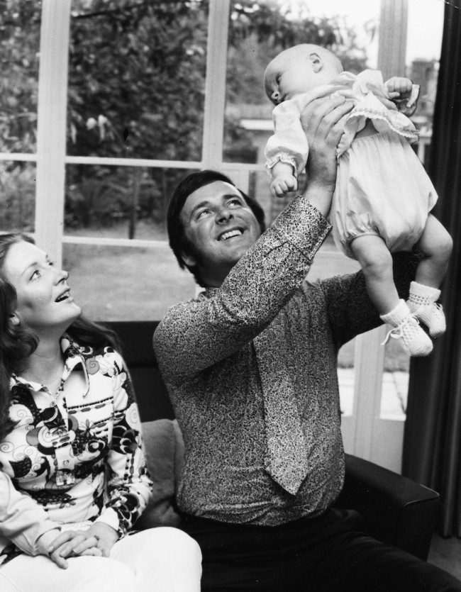 Irish broadcaster Terry Wogan with his wife Helen, holding his baby daughter Katherine in the air at their home, circa 1972. (Photo by Chris Ware/Keystone/Getty Images)